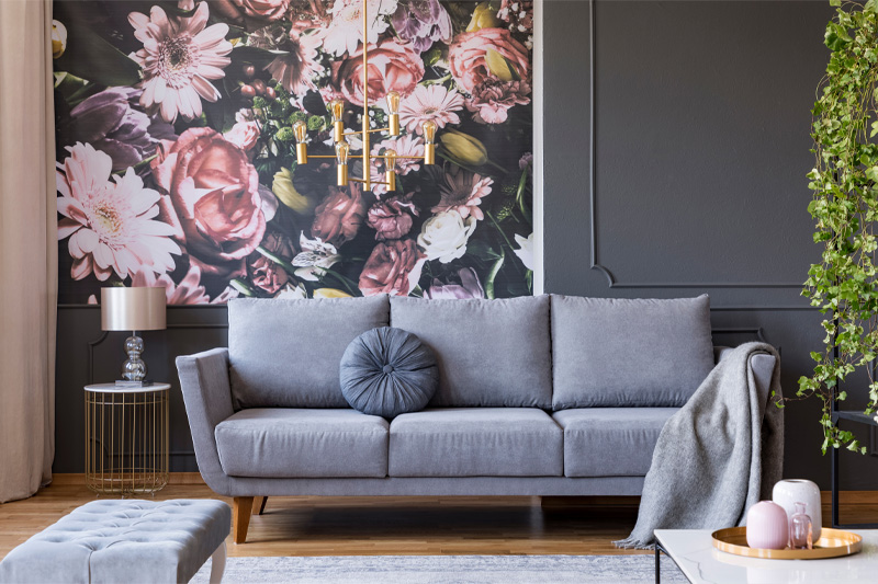 A grey couch in a room with a floral wallpaper
